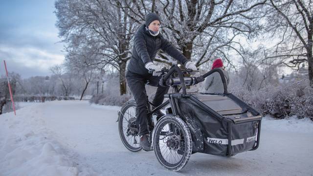 Frau mit Winterkleidung fährt im verschneiten Park mit dem Livelo #1, Standardkorb vorn ist geschlossen